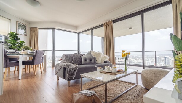 A modern living room with a gray sofa, a coffee table, and a dining area with a table and chairs. - Sky Homes on Queen (Brisbane)
