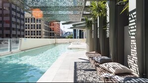 A swimming pool with lounge chairs and a covered area, surrounded by buildings. - Sky Homes on Queen (Brisbane)
