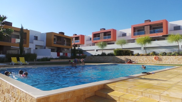 Uma área de piscina com vista clara, escadas de acesso e um edifício com varandas ao fundo.