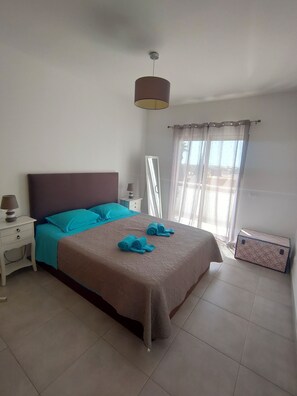 Quarto com cama, mesa de cabeceira, luminária e mala.