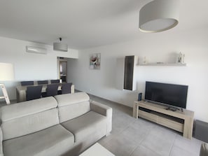 Uma sala de estar moderna com sofá, televisão e área de jantar.