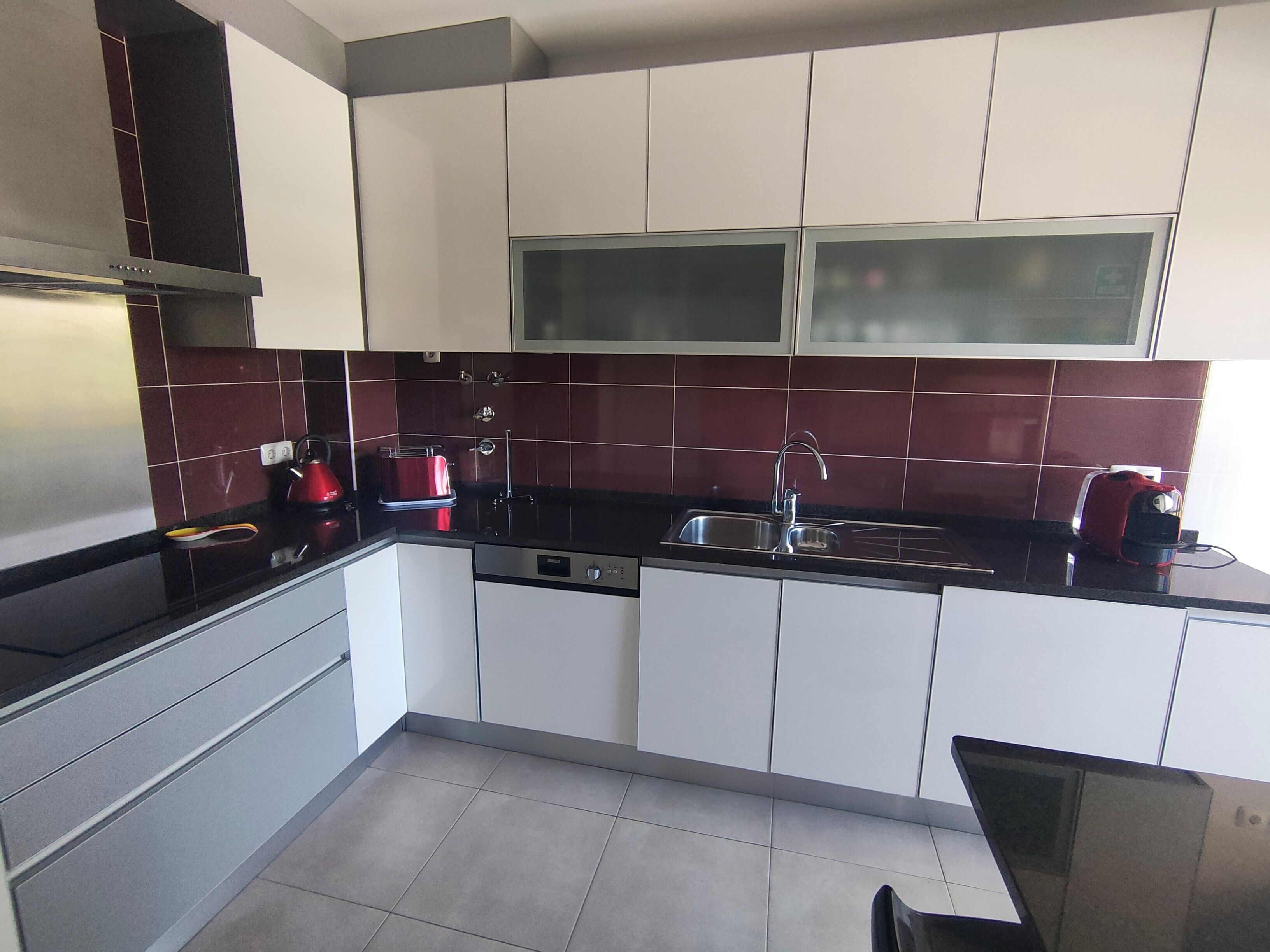 A modern kitchen with white cabinets, a black countertop, and a red kettle.