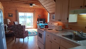 Een gezellig cabin interieur met houten plafond, een eethoek, een keuken met fornuis en broodrooster, en uitzicht door de glazen deur.