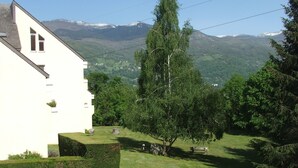 A white building with a sloped roof, a well-maintained lawn, and a large tree in the foreground.