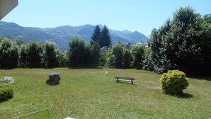 A grassy outdoor area with a table and chairs, a bench, and a small bush.