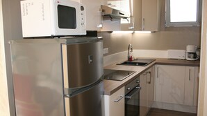 A compact kitchen with stainless steel appliances, a microwave, a sink, and a window above the countertop.