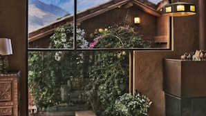 A cozy room with a large window offering a mountain view, a wooden bench, and a glass coffee table with decorative items. - Luxury house in Sacred Valley. Modern comfort, rustic style, stunning views (Urquillos Urubamba)