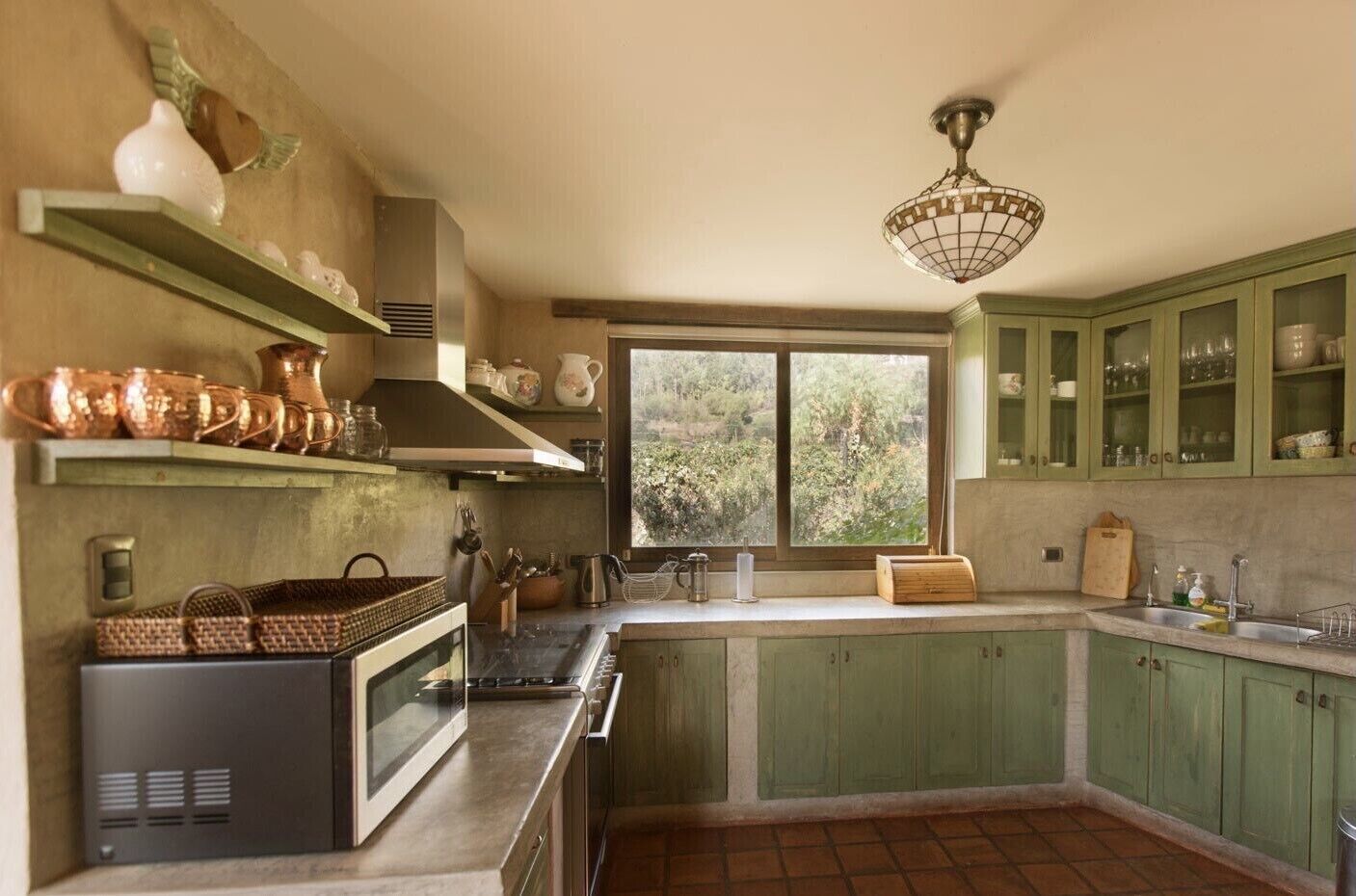 A kitchen with green cabinets, a microwave, a stove, and a window with a view of greenery.