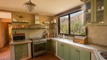 A kitchen with green cabinets, a stove, a microwave, and a window with a view of a mountainous landscape.