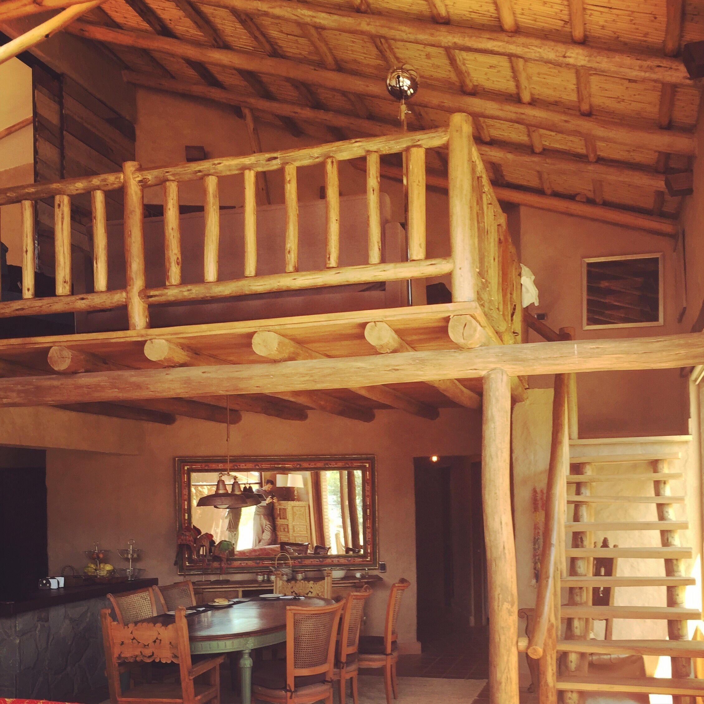 A rustic interior with a wooden staircase, a dining area with a table and chairs, and a chandelier.