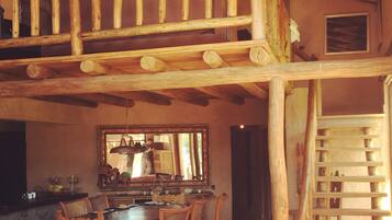A rustic interior with a wooden staircase, a dining area with a table and chairs, and a chandelier.