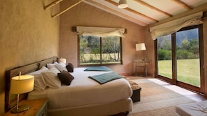 A bedroom with a bed, bedside table, lamp, and large windows. - Luxury house in Sacred Valley. Modern comfort, rustic style, stunning views (Urquillos Urubamba)