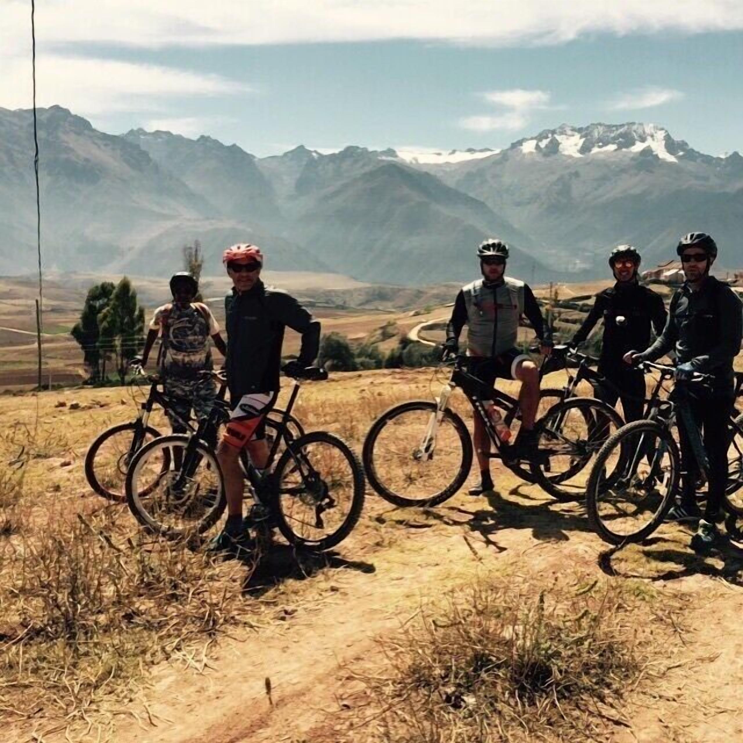 En gruppe cyklister på en grusvej med et bjergrigt landskab i baggrunden.