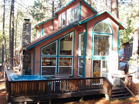 A cabin with a stone chimney, large windows, and a wooden deck.