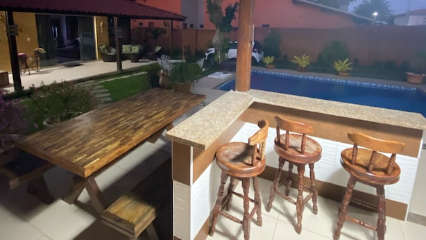 Un espace extérieur aménagé en terrasse, avec une table en bois et des tabourets de bar, une piscine et un coin salon abrité.