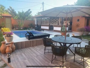 Un espace piscine comprenant un coin détente avec des chaises longues, une table avec des chaises et des plantes en pot.
