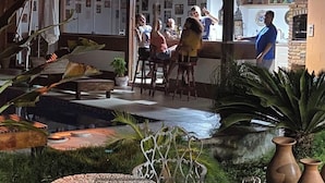Un espace extérieur aménagé avec des sièges, une piscine, des plantes tropicales et un bar doté d’un comptoir.