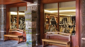 Ein Fitnessraum mit Trainingsgeräten, Holzbänken und steinernen Säulen.
