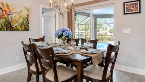 A dining area with a table set for six, a chandelier, and a view of a swimming pool.