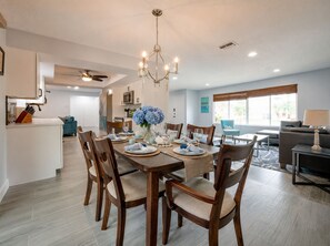 A dining area with a chandelier, wooden chairs, a table set for four, and a kitchen in the background.