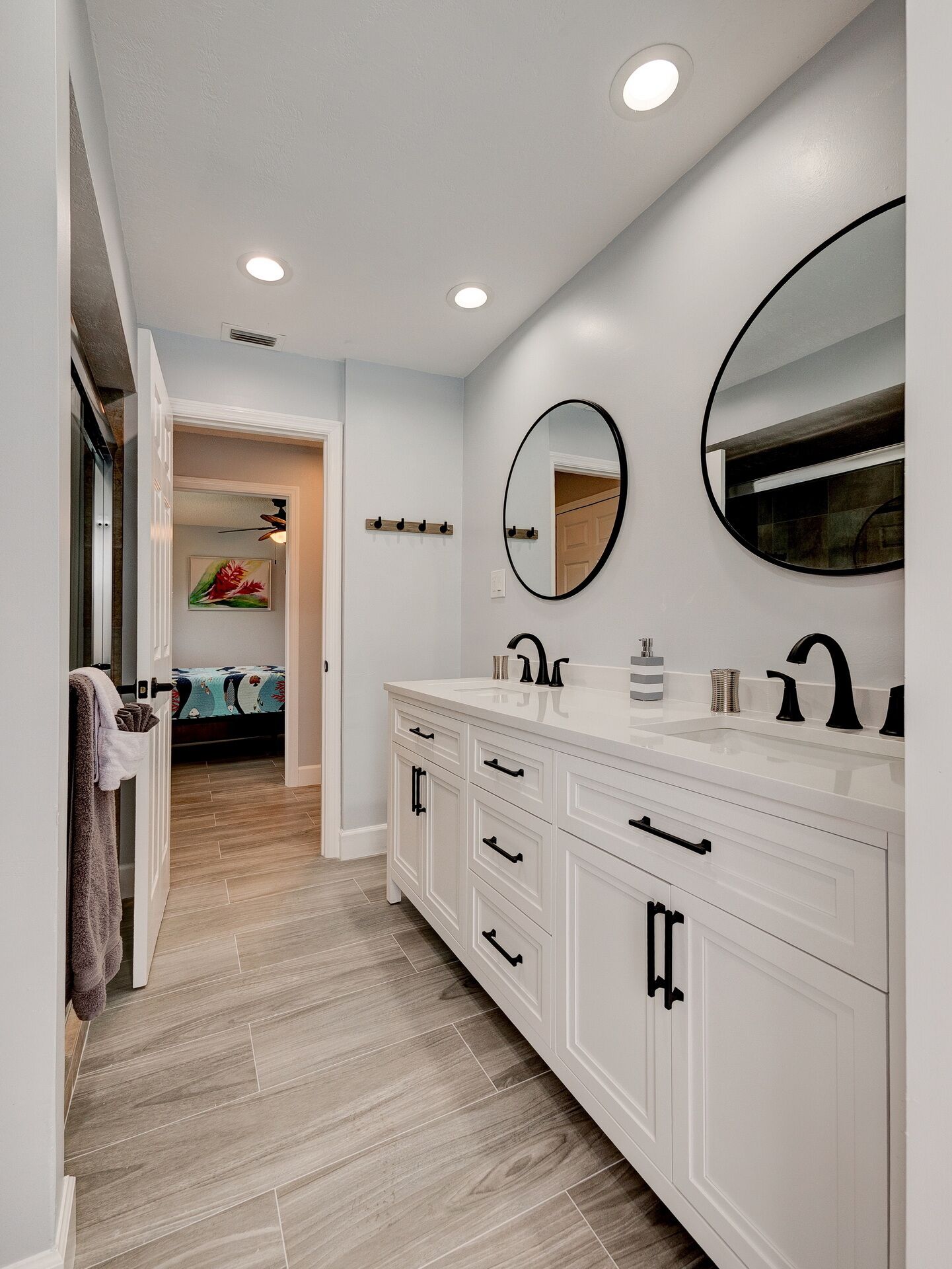 Un baño con muebles blancos, dos espejos y un lavamanos.