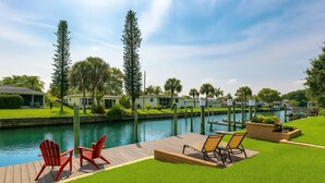 A waterfront property with a wooden deck, red Adirondack chairs, and a grassy lawn.