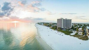 A beachfront hotel with a large building, a sandy beach, and a calm sea.