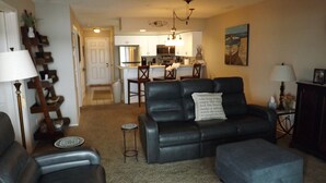 A living room with a sofa, ottoman, and a coffee table. There is a kitchen in the background with a refrigerator, microwave, and dining area. - Fabulous Patio View Overlooking The Main Channel Of Table Rock Lake (Hollister)