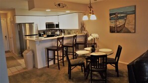A compact kitchen with white cabinets, a stainless steel refrigerator, and a microwave. There is a dining area with a round table and chairs, and a painting on the wall. - Fabulous Patio View Overlooking The Main Channel Of Table Rock Lake (Hollister)