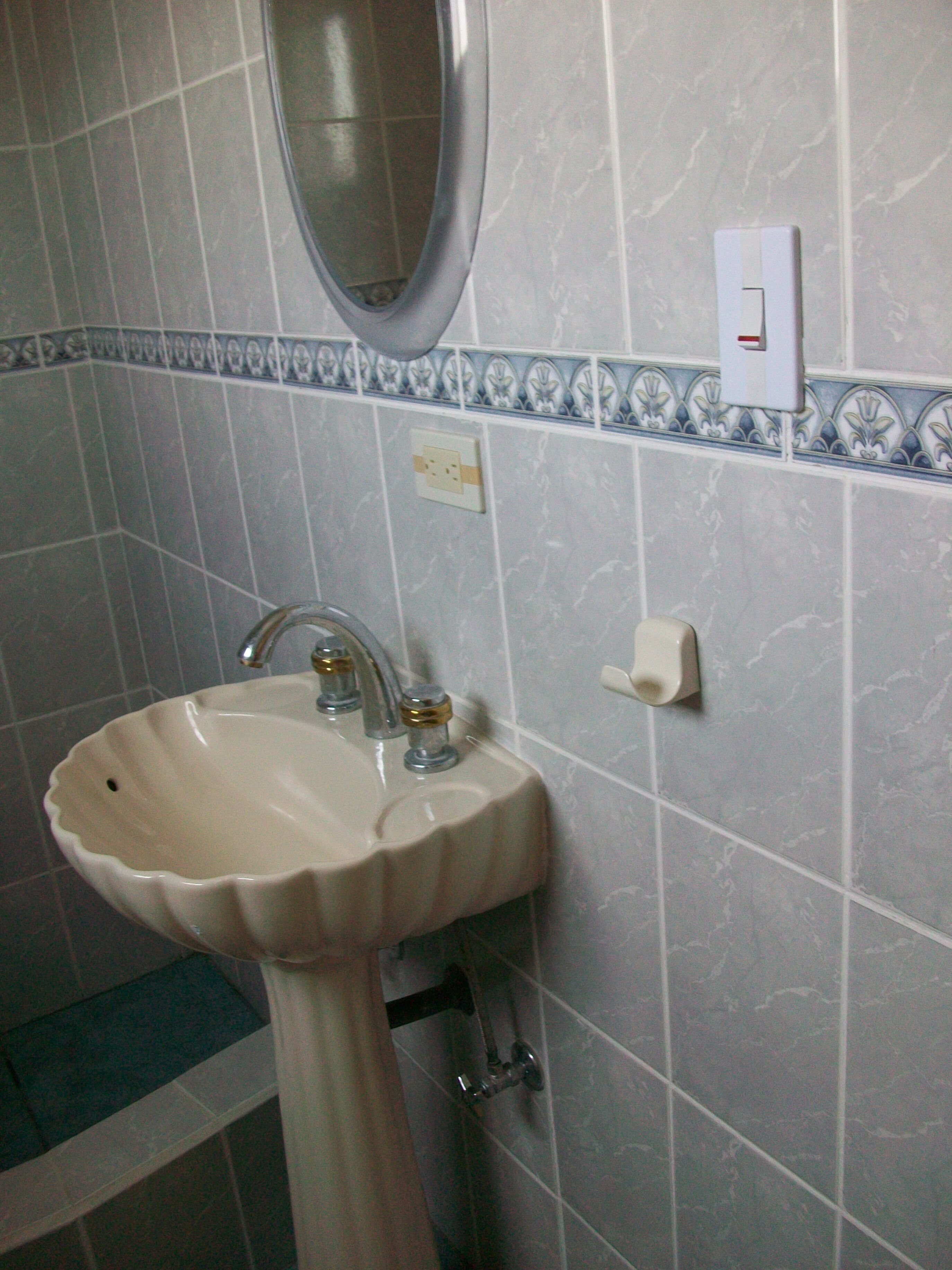 Un baño con lavamanos pedestal, un espejo y dispensador de toallas.