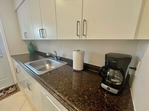 Una cucina con lavello in acciaio inossidabile, dispenser di carta assorbente e macchina da caffè.