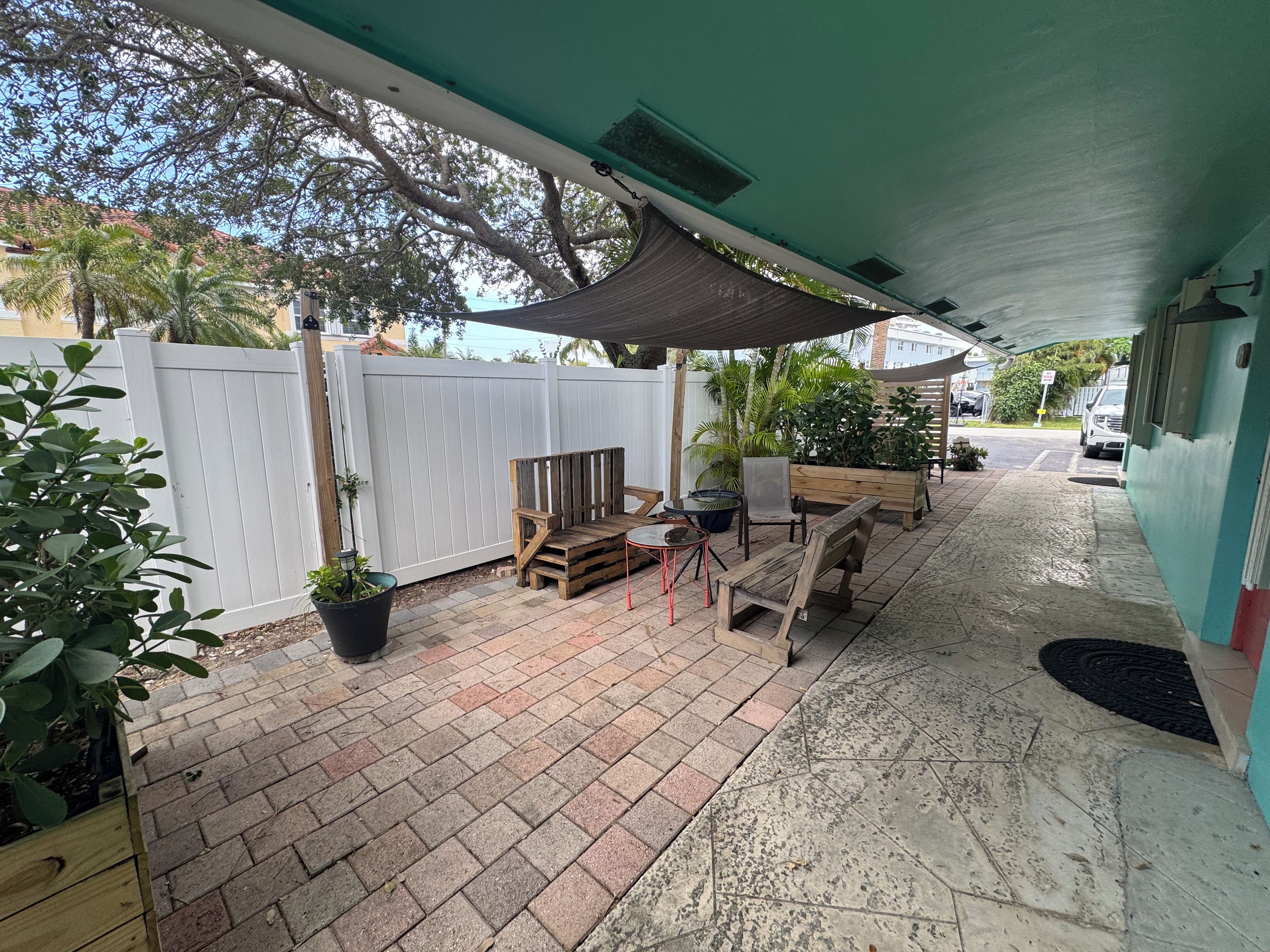 A covered patio area with a white fence, wooden furniture, and potted plants.
