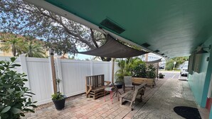 Ein überdachter Patio-Bereich mit weißem Zaun, Holzmöbeln und Topfpflanzen.