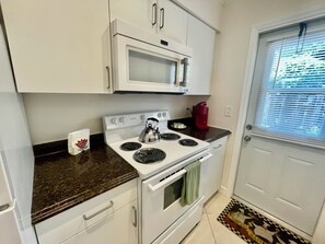 A compact kitchen with white appliances, a microwave, a kettle, and a red coffee maker.