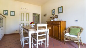 A dining area with a wooden table, white chairs, a wicker chair with a cushion, and a cabinet. - Historical Center With Large Terrace (Lucca)