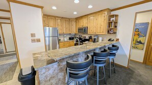 A modern kitchen with wooden cabinets, stainless steel appliances, a granite countertop, and bar stools. - Luxury Condo w/ FREE WiFi, Parking, Heated Pool, Hot Tubs, Skier Shuttles (Avon)