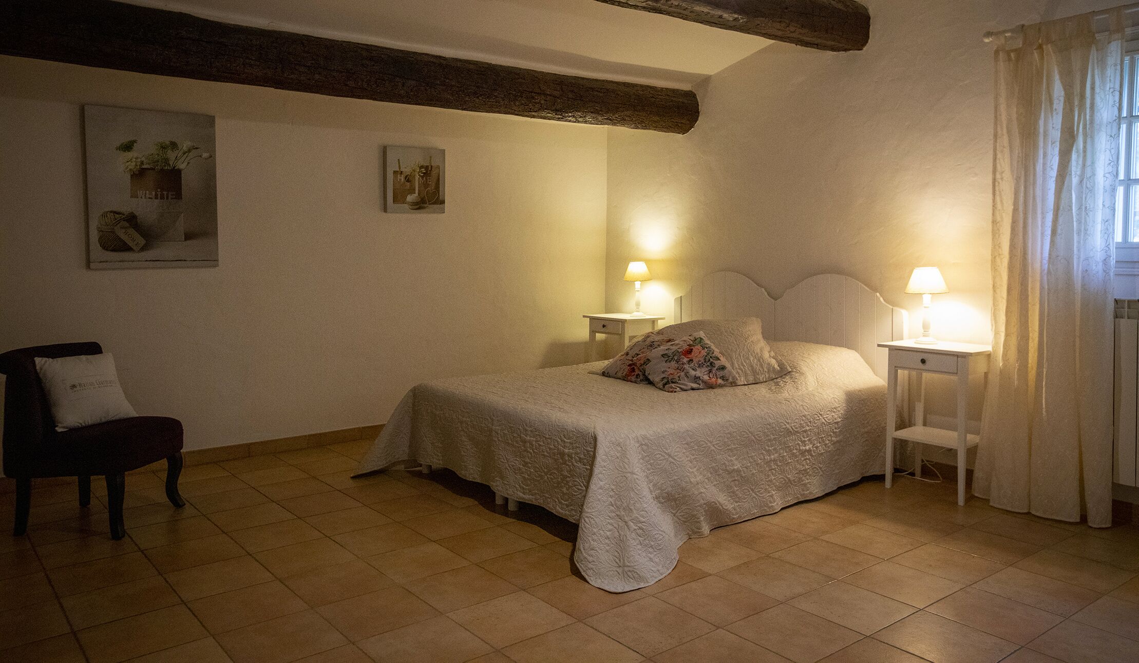 Un dormitorio acogedor con una cama, dos mesitas de noche con lámparas, una silla y una ventana con cortinas.