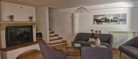 Una sala de estar con chimenea, sofá, sillones, una mesa de centro y una escalera.