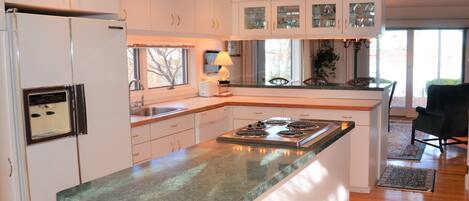 A modern kitchen with white cabinets, a central island with a green countertop, and a built-in stove.