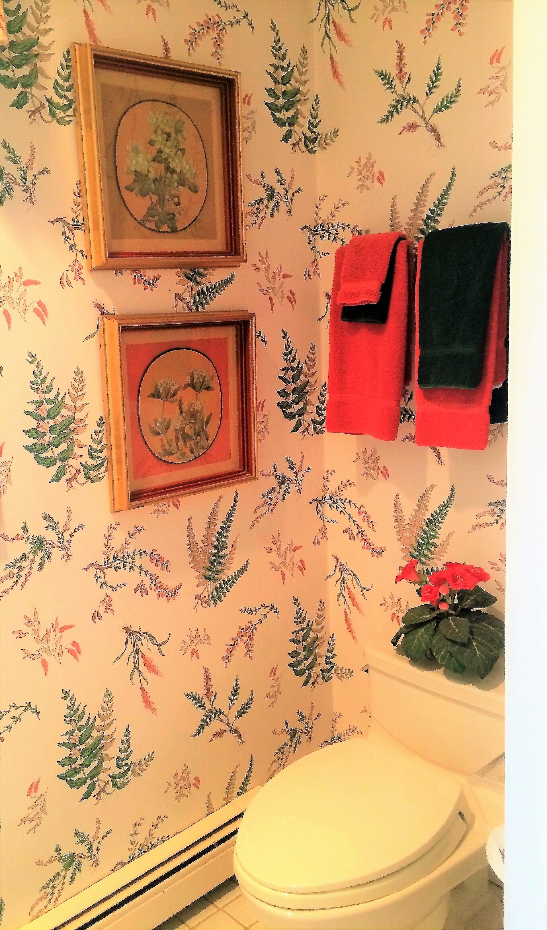 A bathroom with floral wallpaper, two framed pictures, and a toilet.