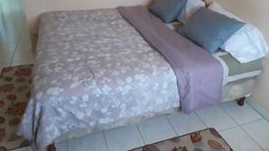 Een bed met een bloemenprintdeken en meerdere kussens, een betegelde vloer en een bloemen gordijn.