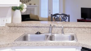 Eine Küche mit Granit Arbeitsplatte, Edelstahlspüle und weißen Schränken.