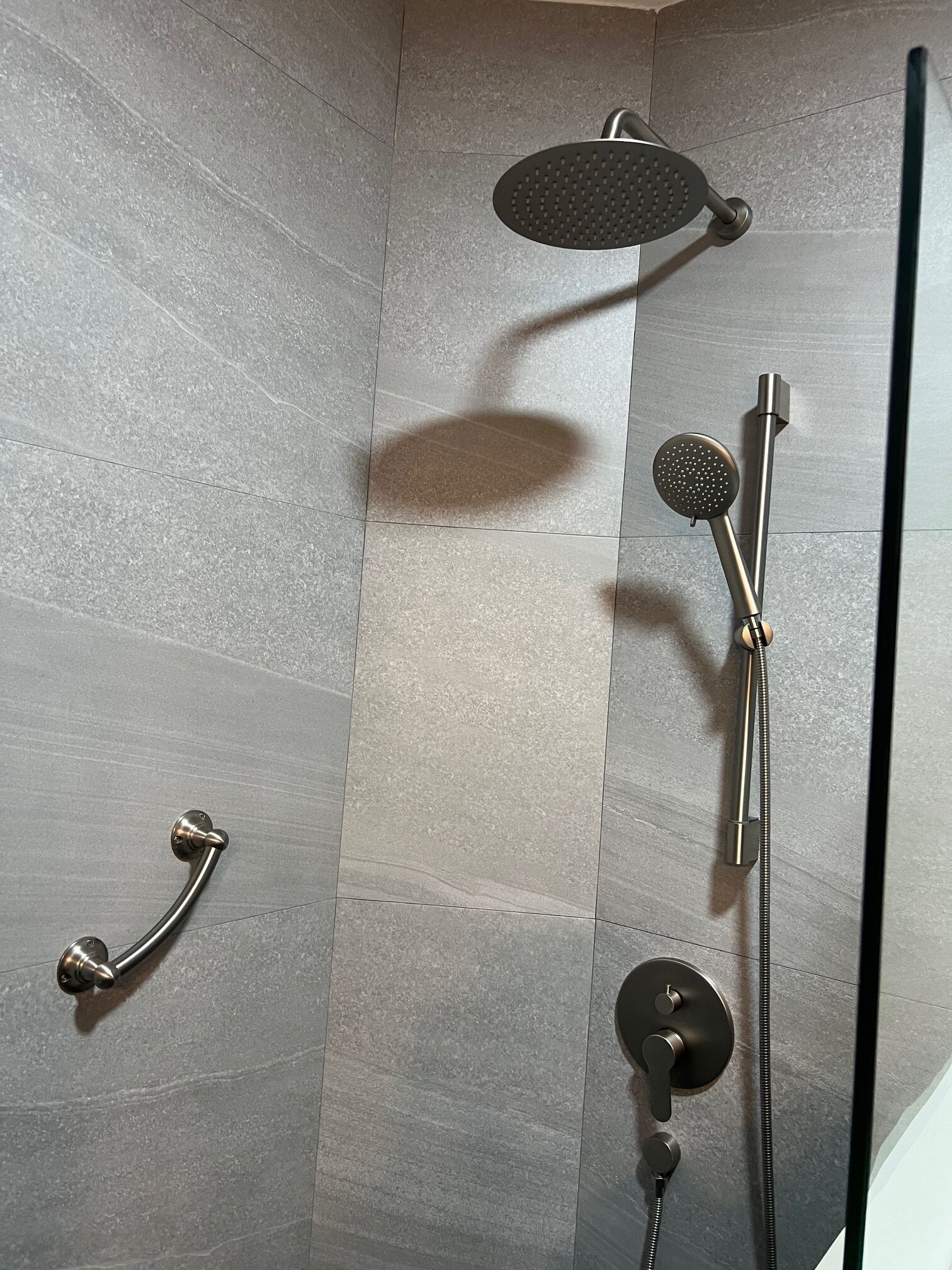 A shower area with a handheld showerhead, a wall-mounted showerhead, and a handheld shower control.