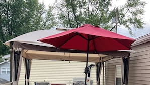 A covered outdoor patio with a table and chairs, a grill, and a red umbrella.