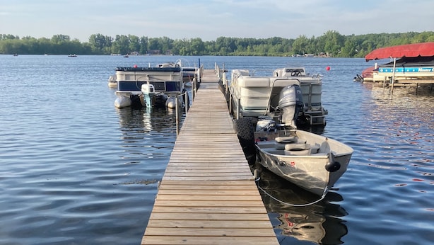 A wooden dock extending into calm water with several boats docked at the end.