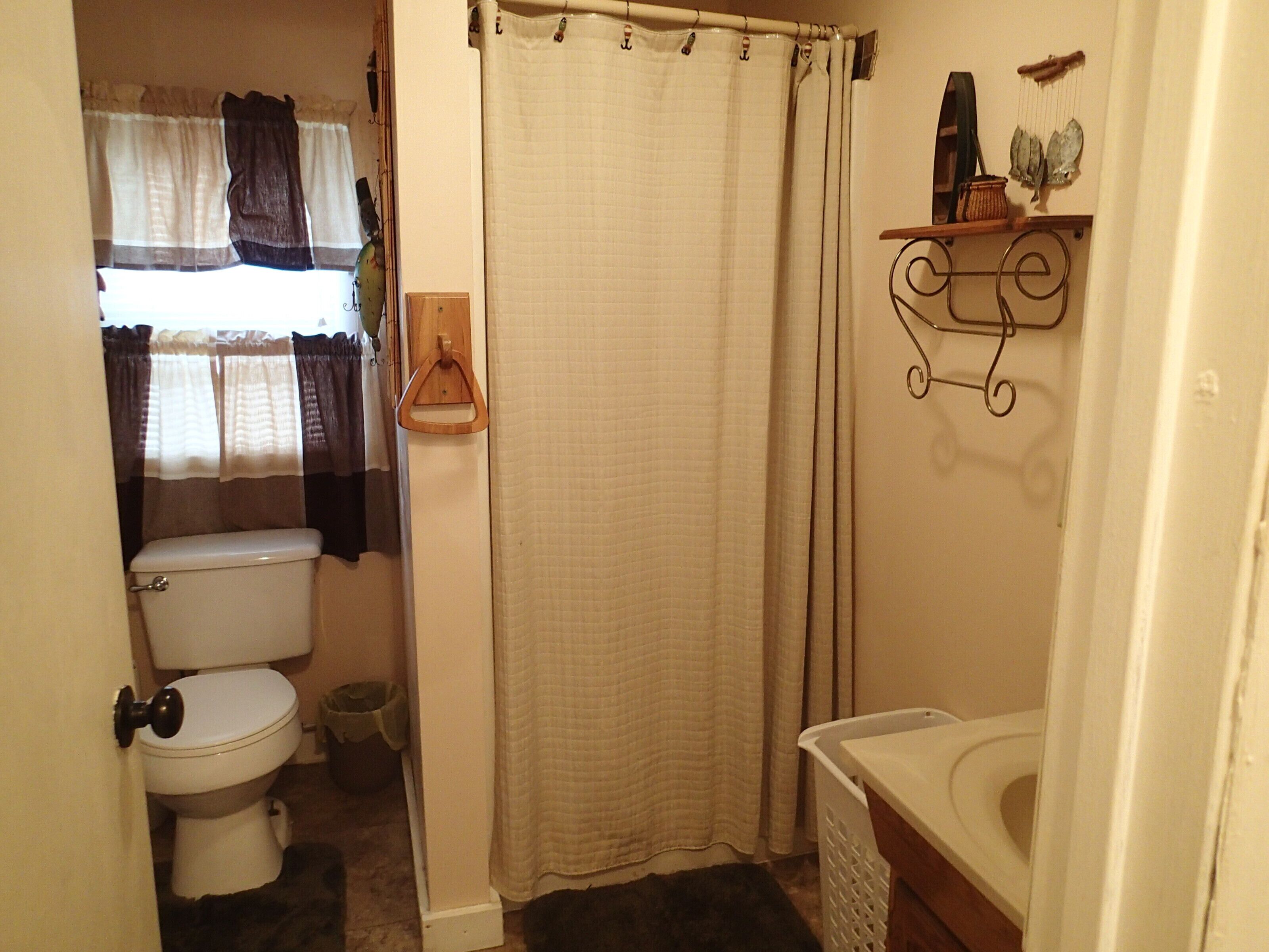 A bathroom with a toilet, a shower curtain, a sink, and a shelf with decorative items.