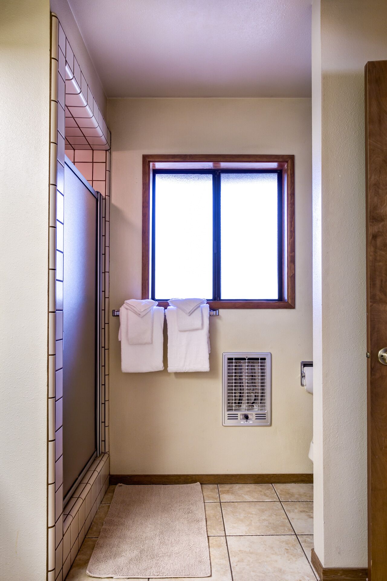 Un baño con ducha, una ventana y dos toallas colgadas en la pared.