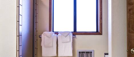 Un baño con ducha, una ventana y dos toallas colgadas en la pared.