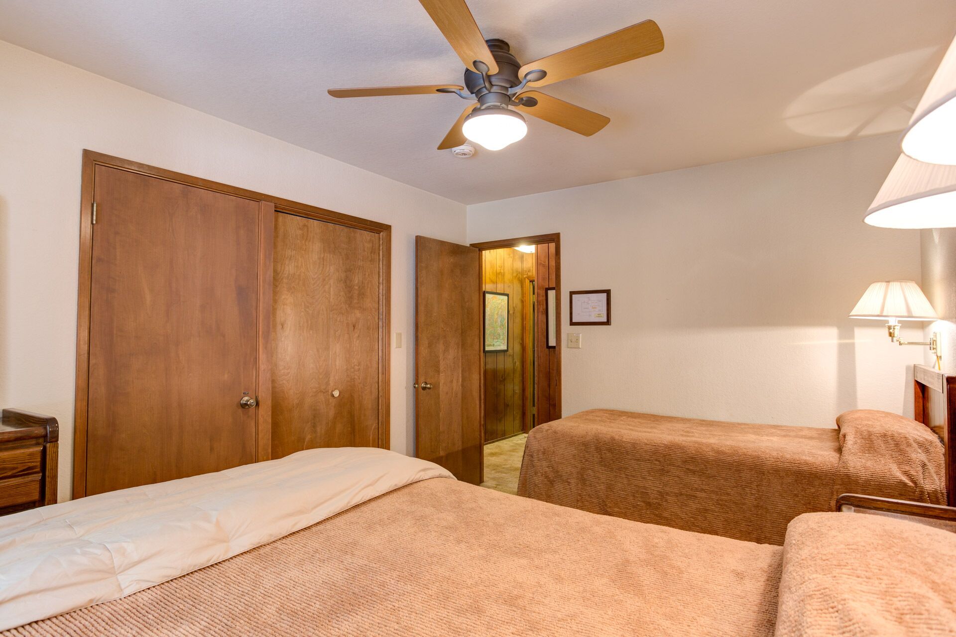 A hotel room with two beds, wooden wardrobes, a ceiling fan, and a nightstand.