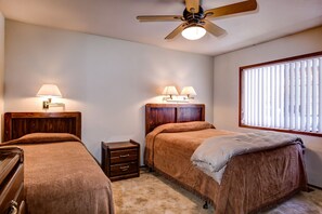 Ein Schlafzimmer mit zwei Betten, Deckenventilator, Nachttischlampen, einem kleinen Nachttisch und einem Fenster mit Jalousien.